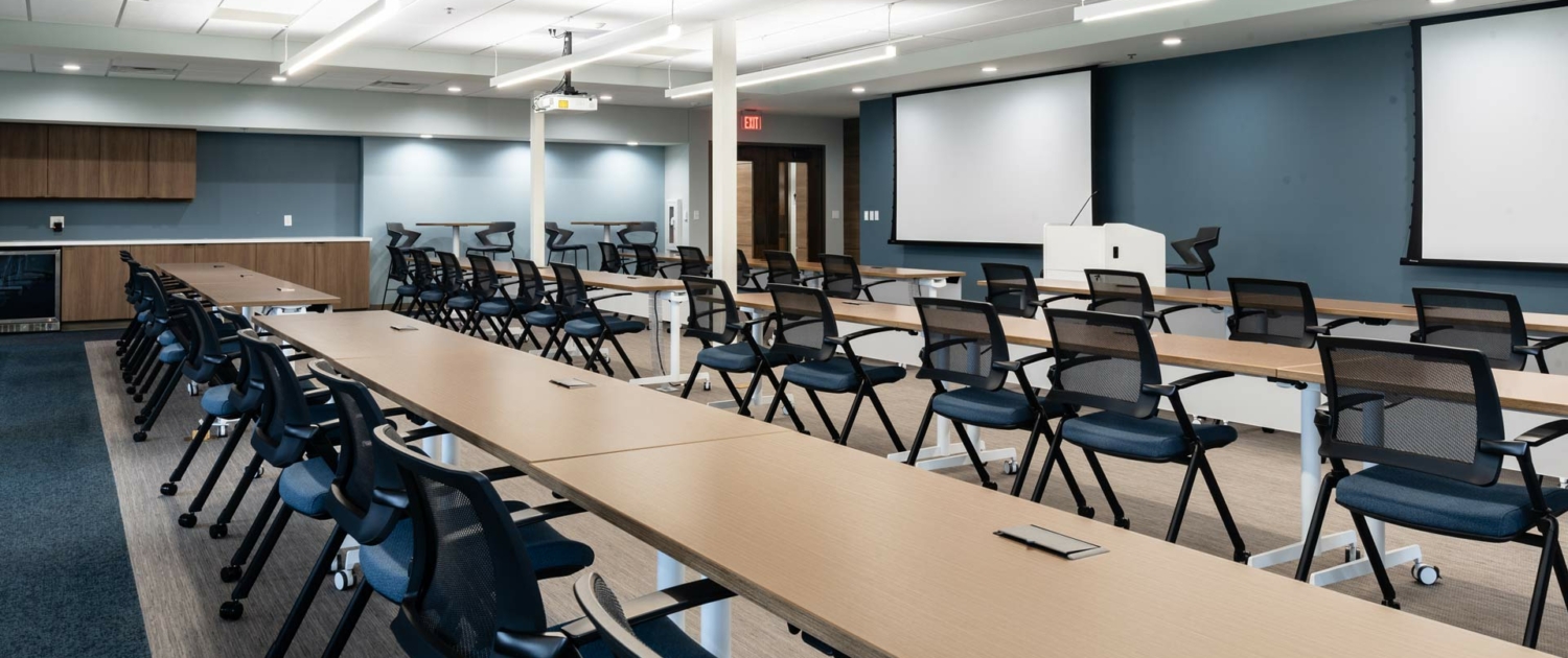 WBA Engagement Center Classroom. Chairs at rows of tables, projector screens in front